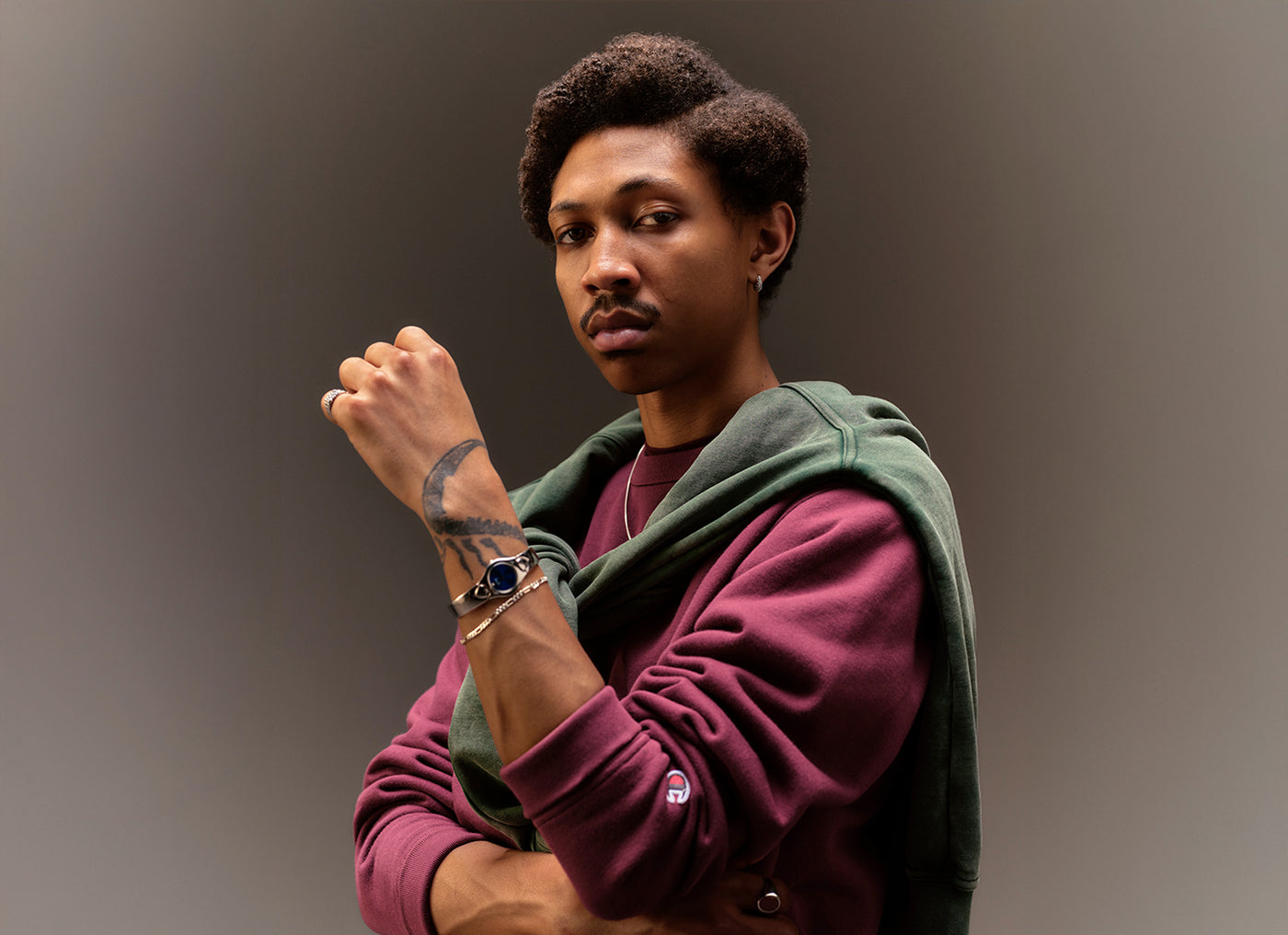 Man wearing a maroon sweatshirt and green sweatshirt overlayed against a gray background