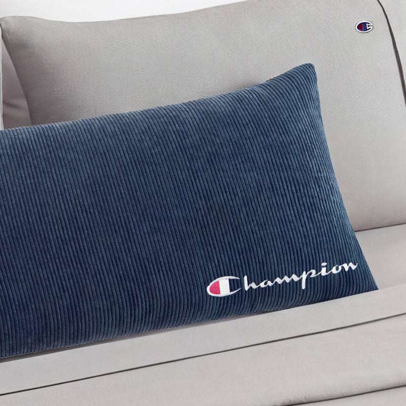 A Champion Corduroy Body Pillow in blue rests on a light gray couch featuring a small Champion logo on the armrest, adding cozy Champion comfort to your lounge space.