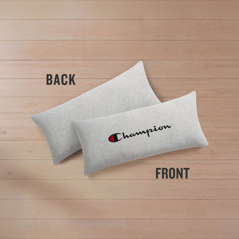 Two light gray rectangular Champion Jersey Body Pillows by Champion rest on a wooden surface. One pillow displays the plain, blank back, while the other showcases the front with "Champion" in bold black script and the signature red and blue Champion logo. Made from soft jersey-knit polyester, these pillows provide full-length cushioning for ultimate comfort—an ideal choice to add stylish support to your space.