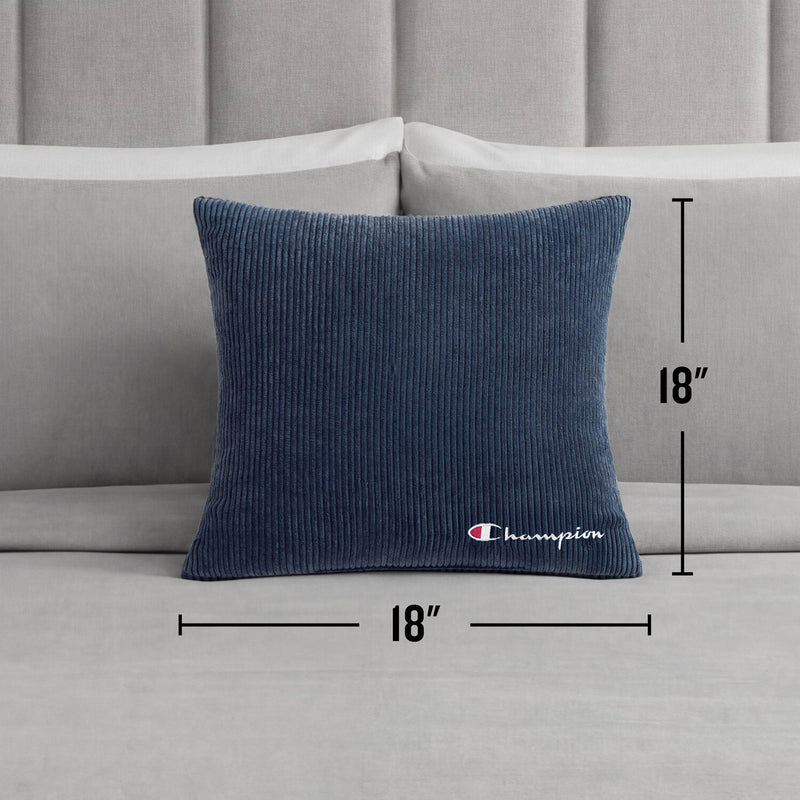 A Champion 18" x 18" Logo Pillow in blue corduroy rests on a light gray bed with a headboard in the background, bringing a casual Champion style to the room.