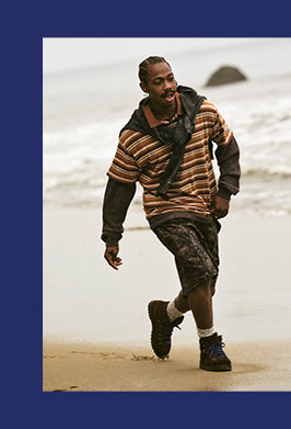 Man walking on a beach wearing a striped sweater and camouflage pants.