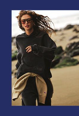 Person wearing a black hoodie and sunglasses on a beach