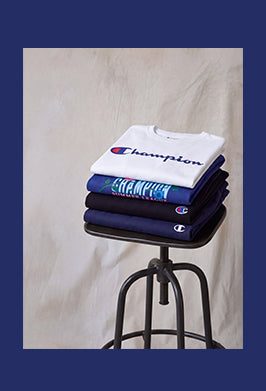 Stack of Champion t-shirts on a black stool against a beige background