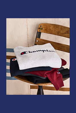 Stack of Champion branded sweatshirts on a wooden chair with a striped cushion.