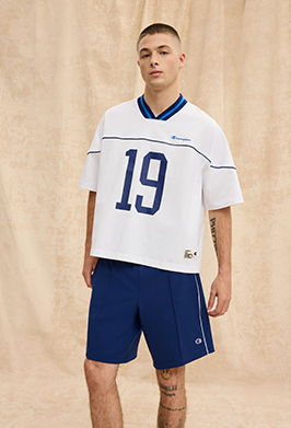 Man wearing a white sports jersey with blue accents and shorts on a beige background