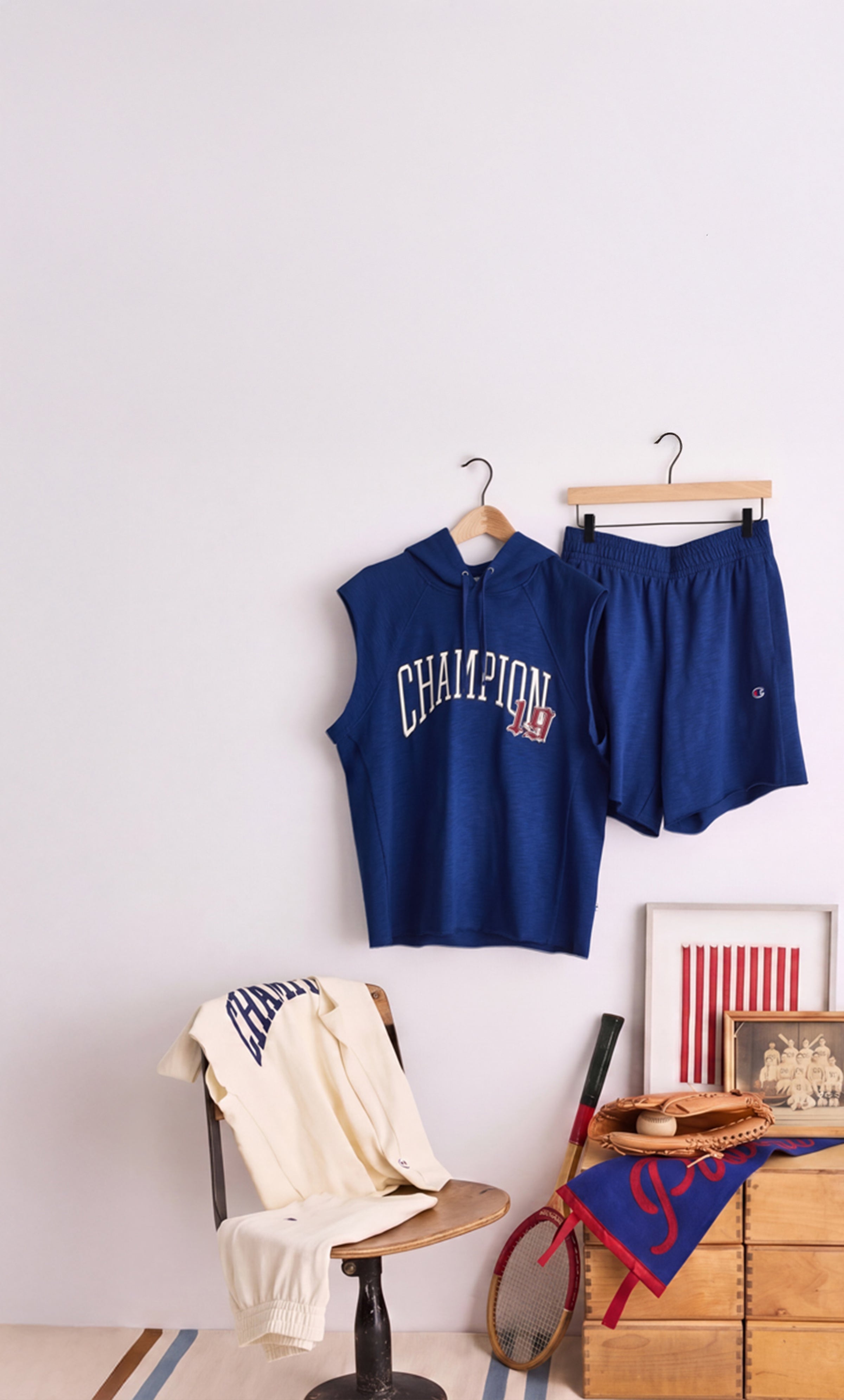 Champion clothing in royal blue and cream tones displayed with vintage sports accessories against a minimalist white backdrop.