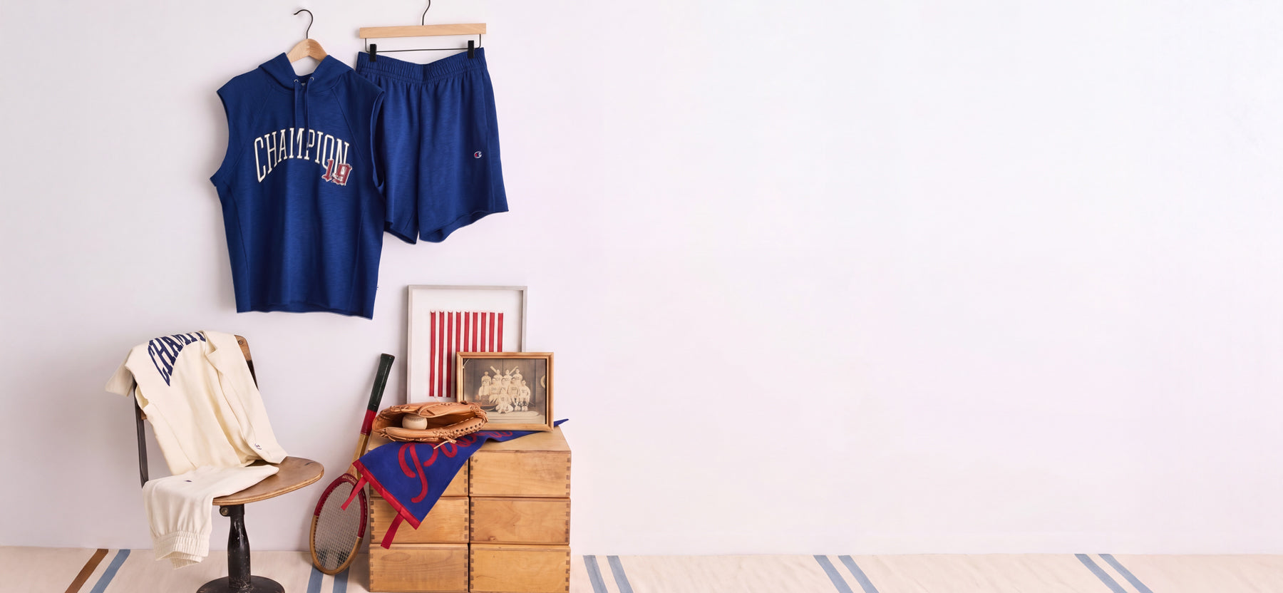 Champion clothing in royal blue and cream tones displayed with vintage sports accessories against a minimalist white backdrop.