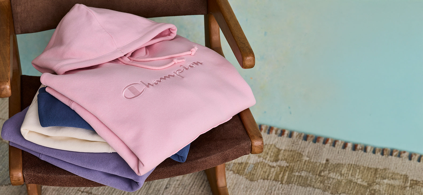 Stack of pink, blue, and white hoodies on a wooden chair against a light blue wall.