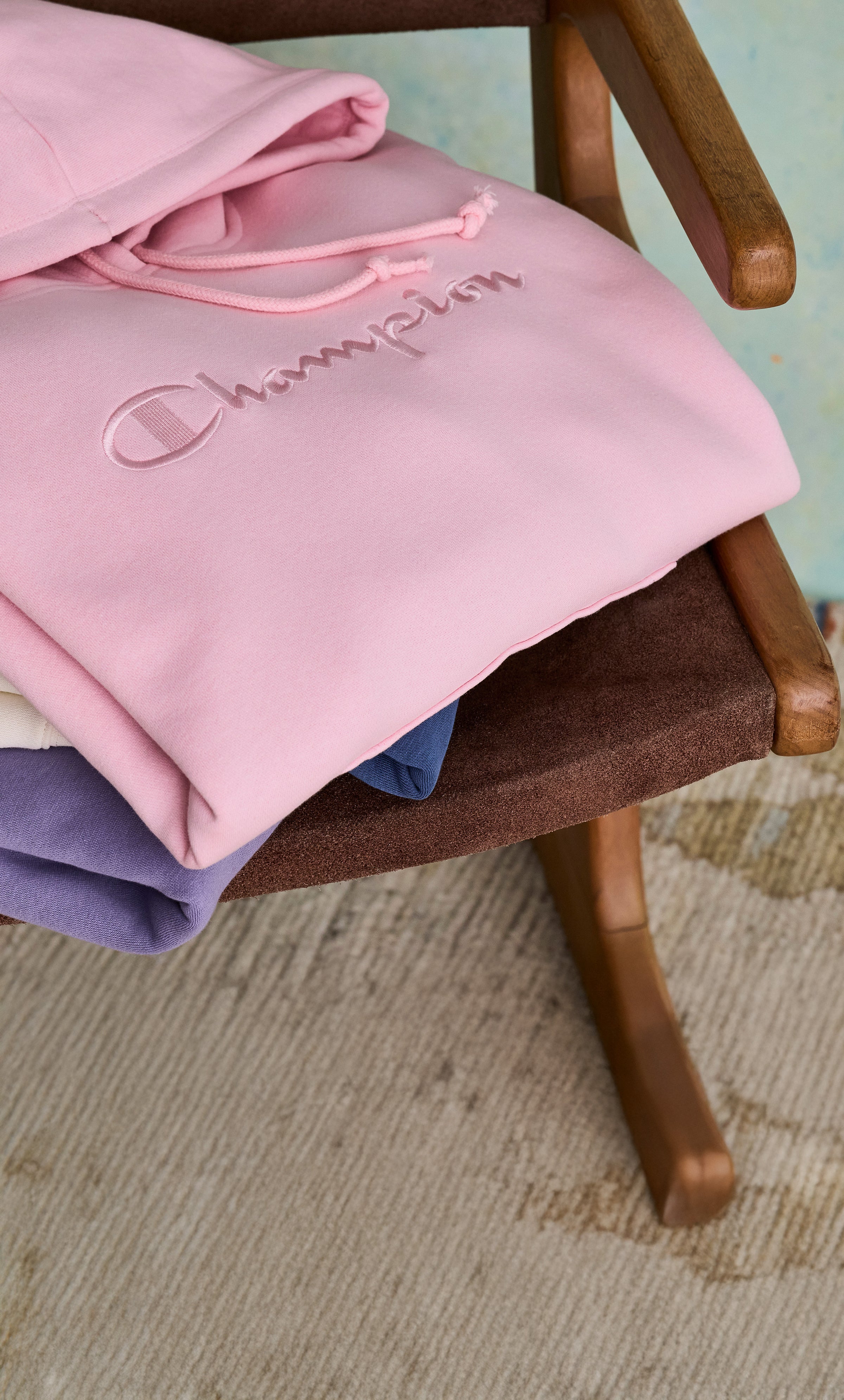 Pink Champion sweatshirt on a wooden chair with a light blue background
