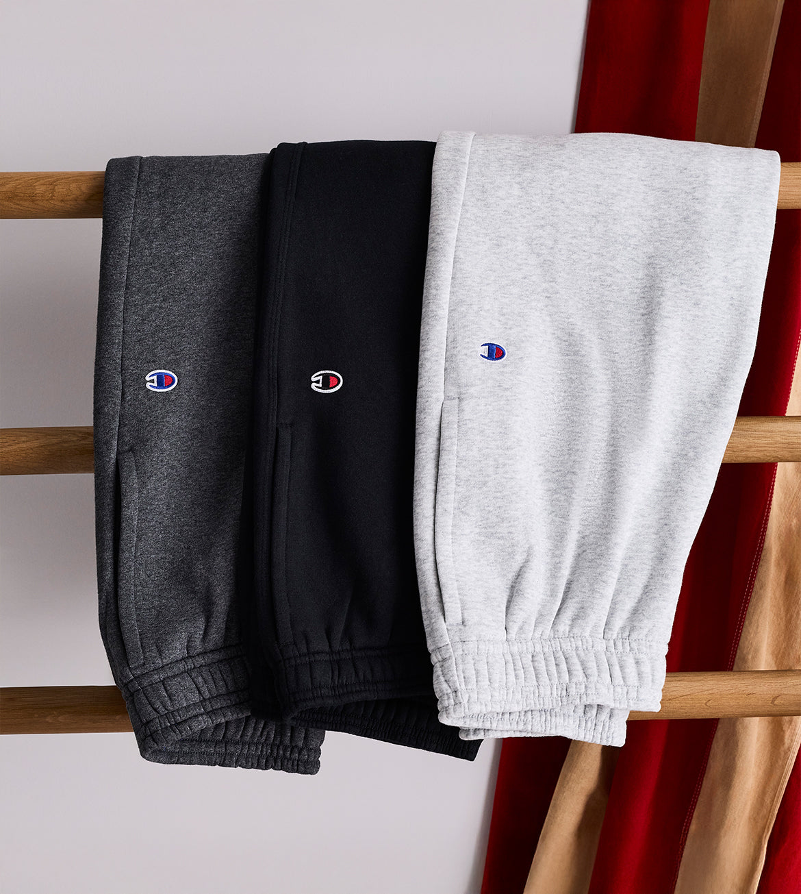 Three pairs of sweatpants in gray, black, and white hanging on a rack.