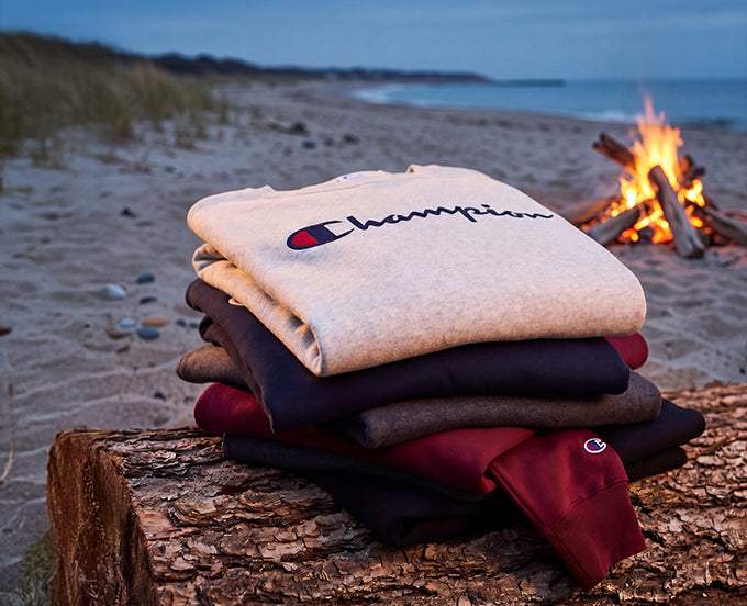 Stack of Champion branded sweatshirts on a log by a beach fire