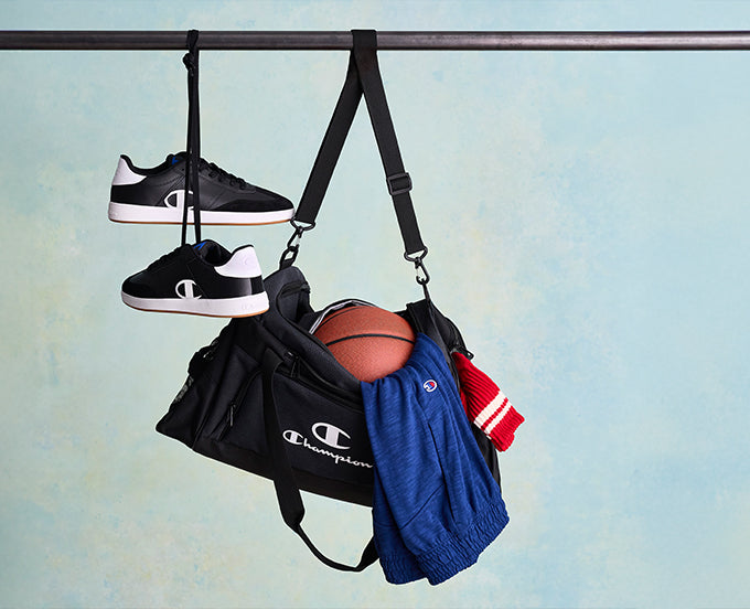 Black Champion bag with shoes, a basketball, and jackets hanging on a rack against a light blue background.