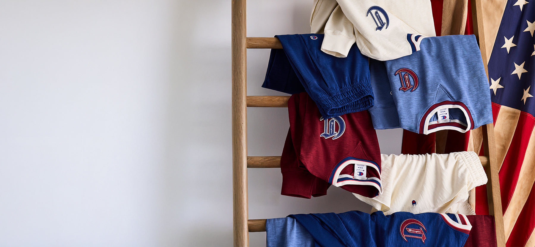 Collection of children's shorts with logos on a wooden ladder against a white wall.