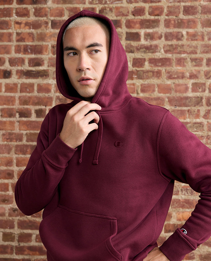 Person wearing a maroon hoodie against a brick wall
