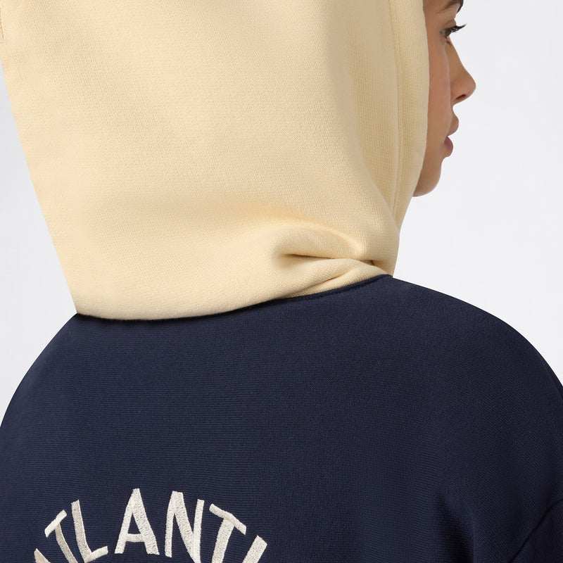 A person photographed from behind and slightly to the side wears a cream hood and a navy Champion Women’s Knitted Hooded Sweatshirt, featuring partially visible white text on the back. The heavyweight fleece material adds extra comfort to this classic Champion hoodie look for women.