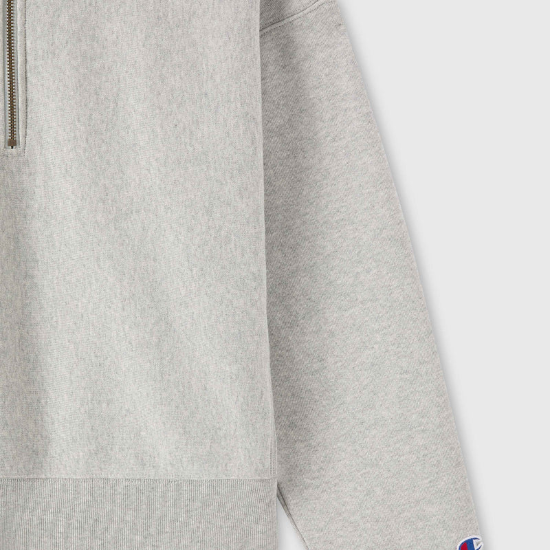 Close-up of a light gray Champion Women’s Knitted Half Zip Sweatshirt with long sleeves. A small patch featuring the blue and red Champion logo is visible on the cuff, highlighting this essential piece of women’s sportswear.
