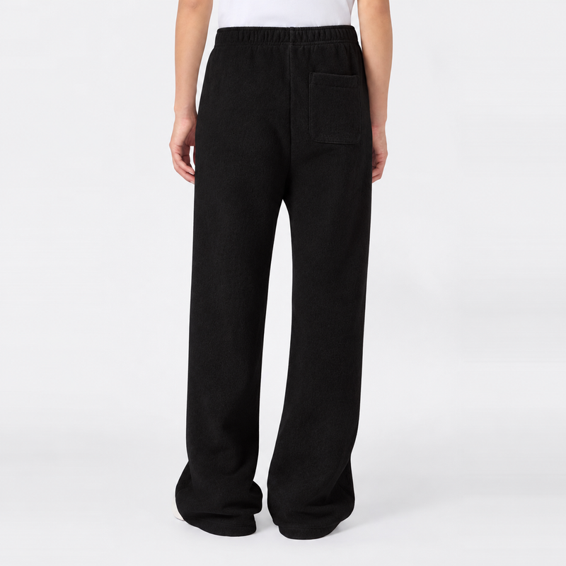 A person is seen from the waist down, standing against a plain white background, wearing Champion Women’s Knitted Flare Pants—loose-fitting black trousers featuring an elastic waistband and back pocket for a modern twist on classic sportswear style.