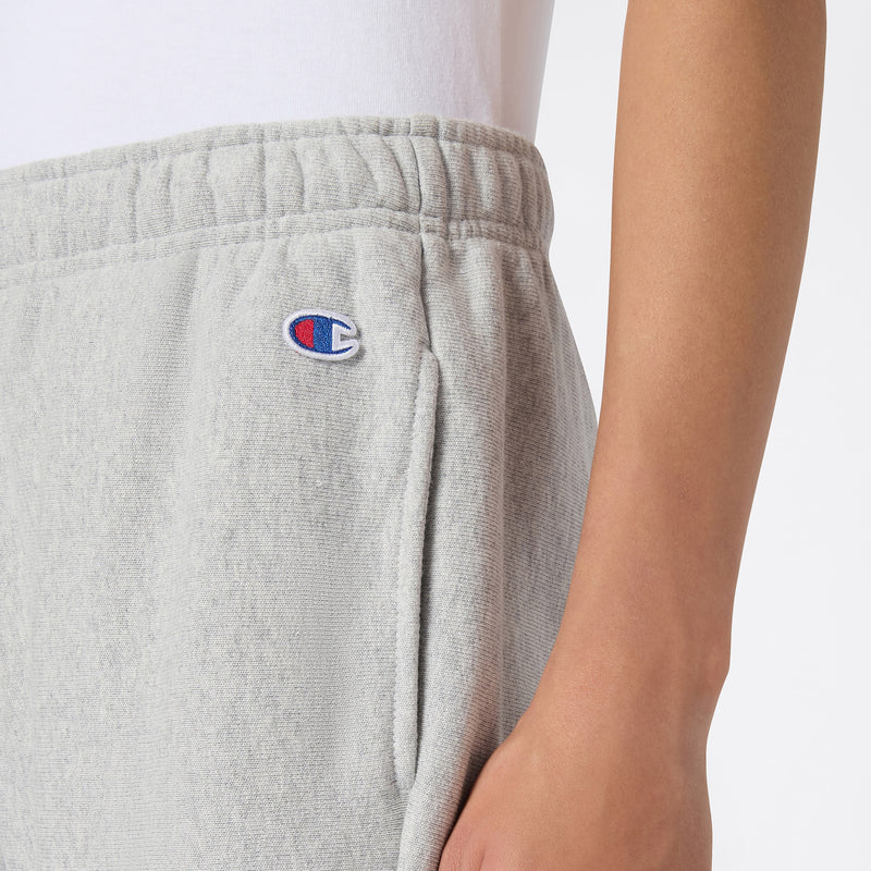 A close-up of a person wearing light gray Champion Women’s Knitted Flare Pants, featuring the iconic logo near the pocket and crafted from soft knit fabric. The pants are paired with a white shirt, and the person’s right arm is visible alongside the pants, highlighting this stylish update to women’s flared sportswear.