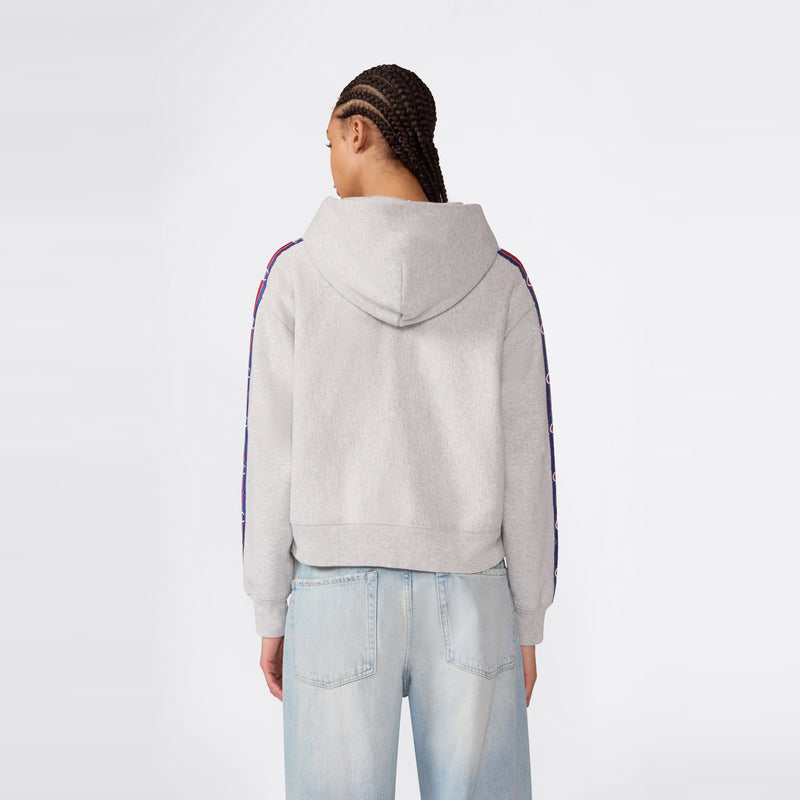 A person with braided hair is standing with their back to the camera against a plain background, wearing light blue jeans and a light gray Champion Women’s Icon Hooded Full Zip Sweatshirt featuring patterned stripes on the sleeves.