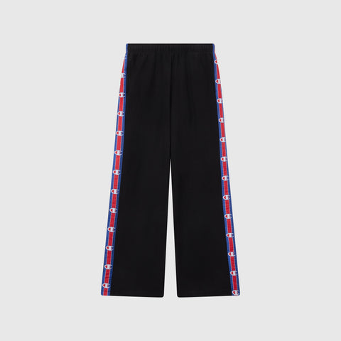 Women’s Knitted Wide Leg Pants by Champion in black, featuring blue and red striped side panels with repeated Champion logos. These pants have a relaxed fit, an elastic waistband, and are photographed against a plain light gray background.