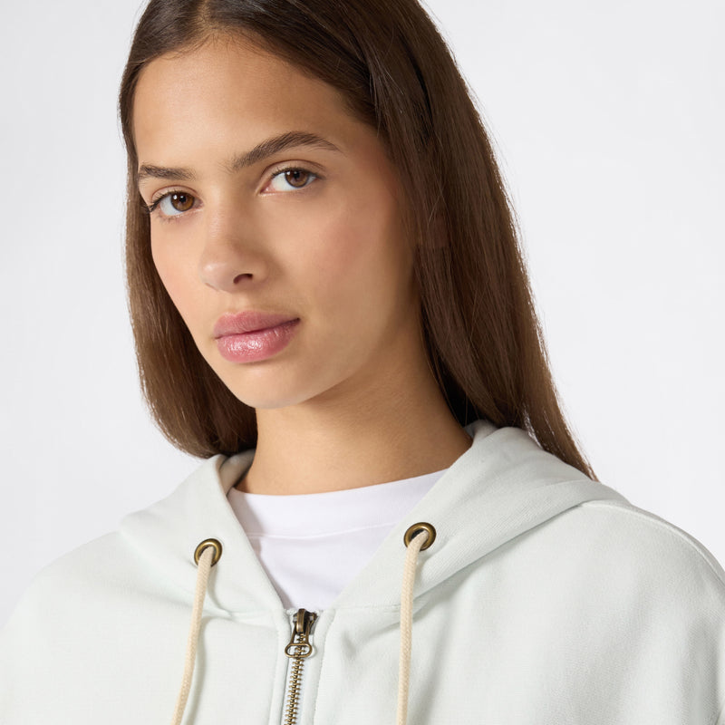 A woman with straight brown hair wears the Champion Women’s Knitted Hooded Full Zip Sweatshirt over a white t-shirt, looking slightly to the side against a plain light background.