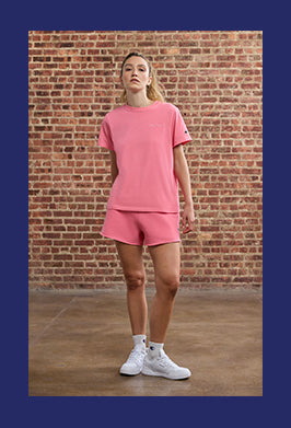 Person wearing a pink outfit standing against a brick wall.