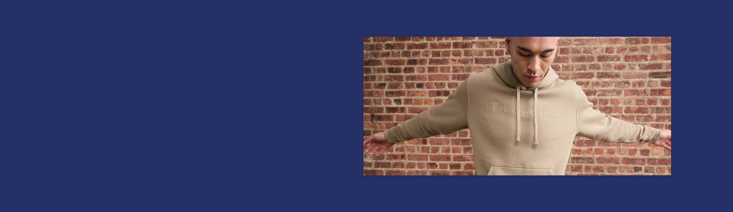 Man wearing a beige hoodie in front of a brick wall