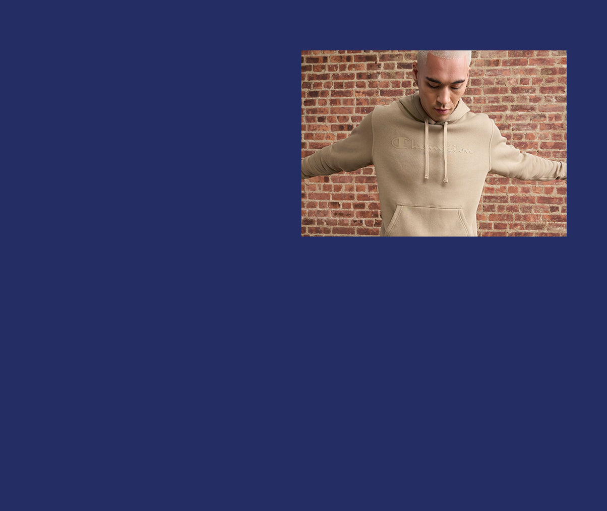 Man wearing a beige hoodie in front of a brick wall on a blue background