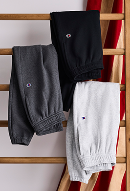 Three pairs of sweatpants in black, gray, and white hanging on a wooden rack.