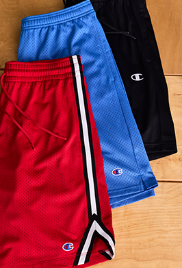 Three pairs of Champion brand shorts in red, blue, and black on a wooden surface.