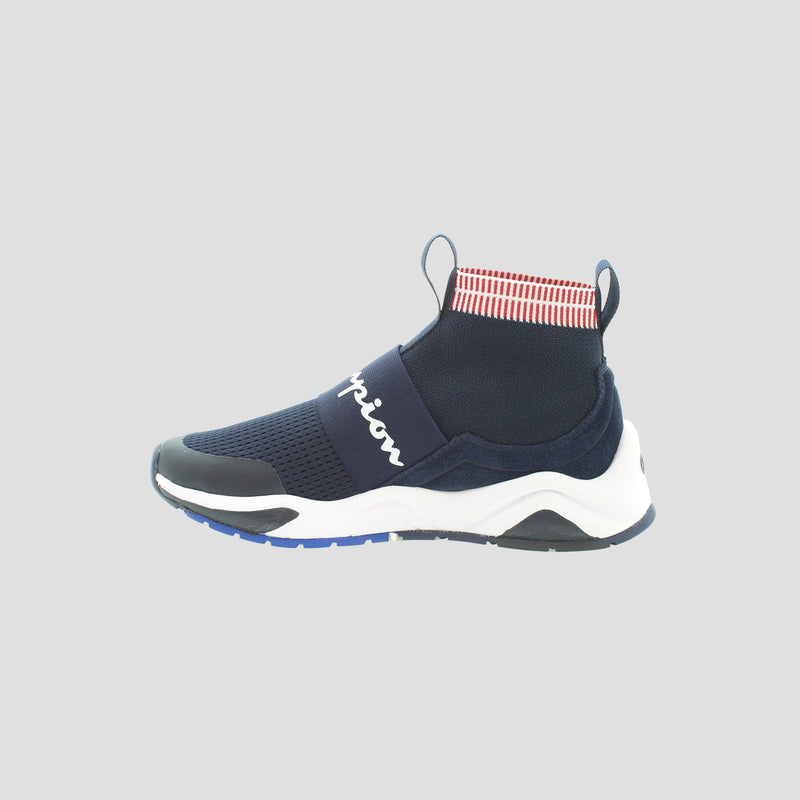 The Champion Kids' Rally Pro is a navy blue knit sneaker with a white sole, black accents, a wide strap with “Champion” in white, and a red-and-white striped ankle collar, shown on a light gray background.