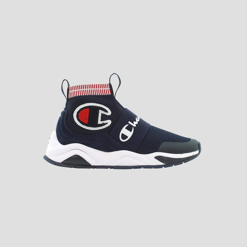 The Champion Kids' Rally Pro is a navy blue slip-on sneaker with a white sole, knit ankle collar with red and white stripes, bold Champion “C” logo on the side, and “Champion” across the upper.