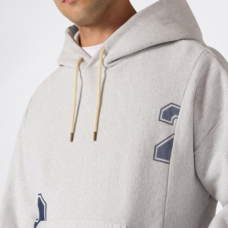 A person wearing a light gray Champion Men’s Knitted Hooded Sweatshirt (College Graphic), featuring tan drawstrings and a blue number 2 printed on the chest. Made with Reverse Weave fleece, this college-inspired hoodie is pictured in an image showing the upper body and part of the face.