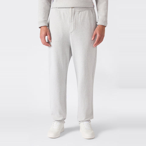 A person is shown from the waist down wearing Champion Men’s Knitted Elastic Cuff Pants in light gray, paired with white sneakers, standing against a plain white background.