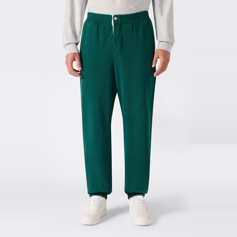A person wearing Champion Men’s Knitted Elastic Cuff Pants in green, paired with a light gray Reverse Weave fleece sweatshirt and white sneakers, stands against a plain white background.