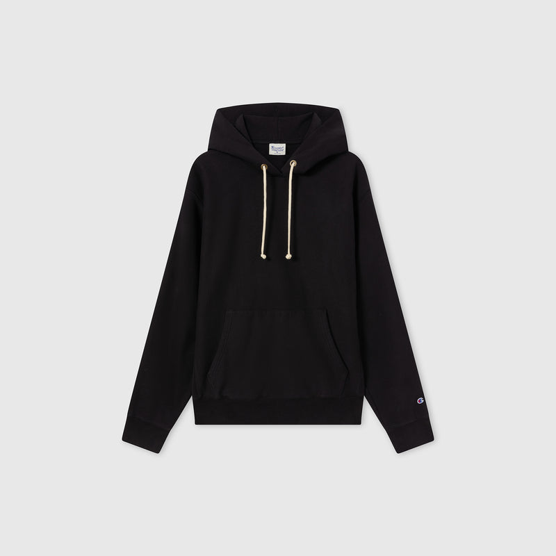 The Champion Men’s Relaxed Fit Hooded Sweatshirt is shown on a light gray background. This plain black hoodie features cream-colored drawstrings, a front pocket, and a subtle logo on the left sleeve. Made from heavyweight fleece, it offers extra warmth and durability.