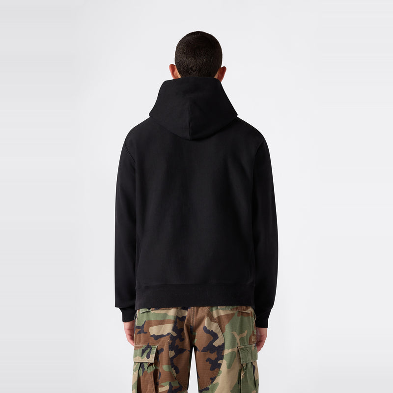 A person stands facing away, wearing the Champion Men’s Relaxed Fit Hooded Sweatshirt and camouflage cargo pants against a plain light background.