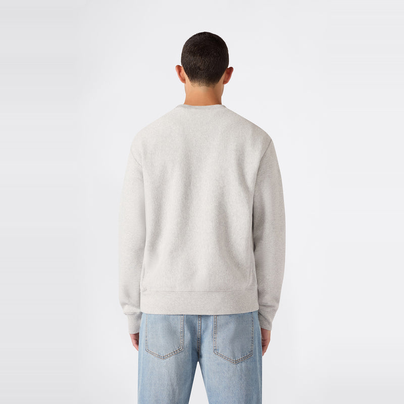 A person with short dark hair is pictured from behind, wearing a light gray Champion Men’s Relaxed Fit Crewneck Sweatshirt and light blue jeans against a plain white background.