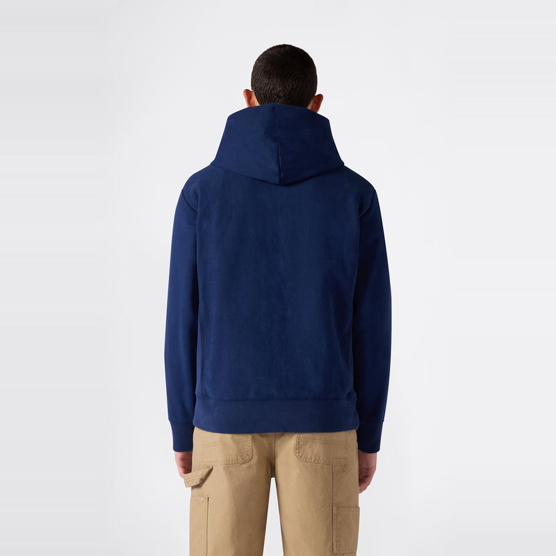 A person wearing a navy blue Champion Men’s Knitted Hooded Sweatshirt (Embroidered Logo) and tan cargo pants stands facing away from the camera against a plain white background.