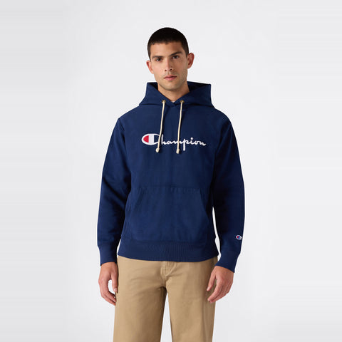A person wearing a navy blue Champion Men’s Knitted Hooded Sweatshirt (Embroidered Logo) paired with beige pants stands against a plain white background.