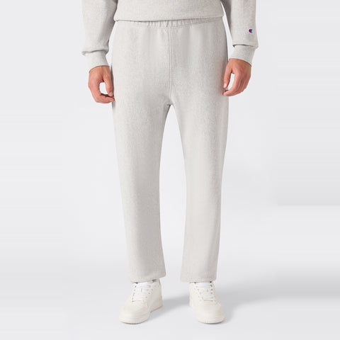 A person wearing light gray Champion Men’s Knitted Elastic Cuff Pants, a matching sweatshirt, and white sneakers stands against a plain white background.