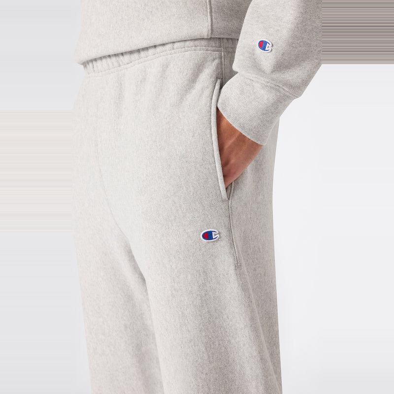 A person wearing light gray Champion Men’s Knitted Elastic Cuff Pants and a matching Relax Core fit sweatshirt with their right hand in the pocket, featuring the Champion logo on both garments.