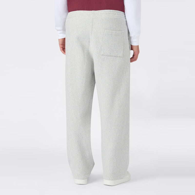 A person wearing light gray Champion Men’s Knitted Wide Leg Pants, featuring a single back pocket, paired with a white shirt and a maroon vest, is shown standing against a plain white background with their back facing the camera.