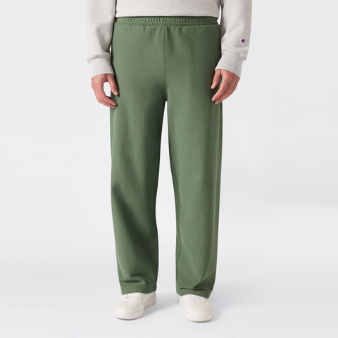 A person is shown from the waist down, standing against a plain light background and wearing loose-fitting green Champion Men’s Knitted Wide Leg Pants, a light gray sweatshirt, and white sneakers.