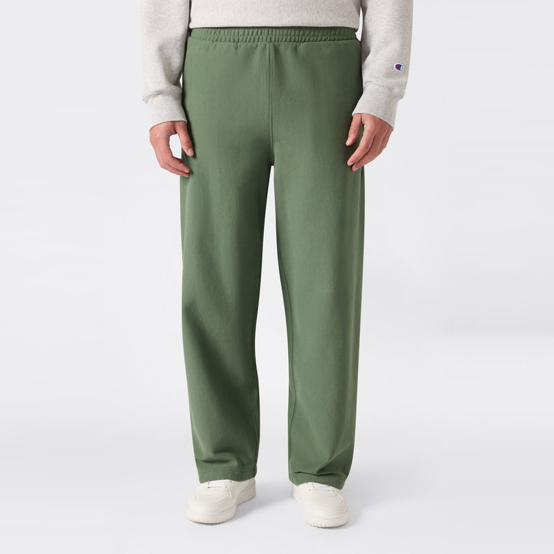 A person is shown from the waist down, standing against a plain light background and wearing loose-fitting green Champion Men’s Knitted Wide Leg Pants, a light gray sweatshirt, and white sneakers.
