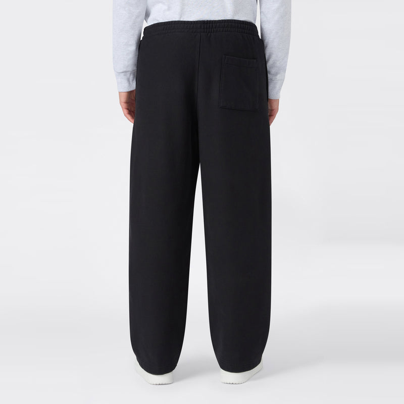 A man wearing Champion Men’s Knitted Wide Leg Pants, featuring a loose fit, elastic waistband, and a single back pocket, stands with his back to the camera against a plain white background.