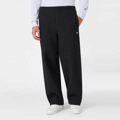 A person is wearing Champion Men’s Knitted Wide Leg Pants in black, paired with a light gray long-sleeve top and white sneakers, standing against a plain white background.