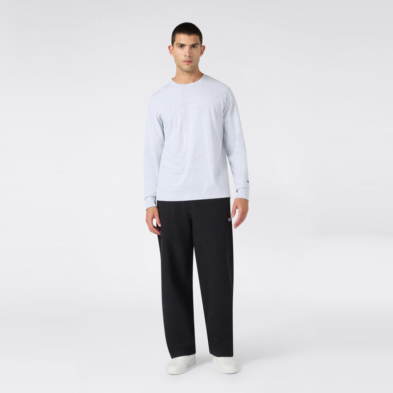 A man stands facing forward, wearing a light gray long-sleeve shirt, Champion Men’s Knitted Wide Leg Pants in black, and white shoes, against a plain light background.