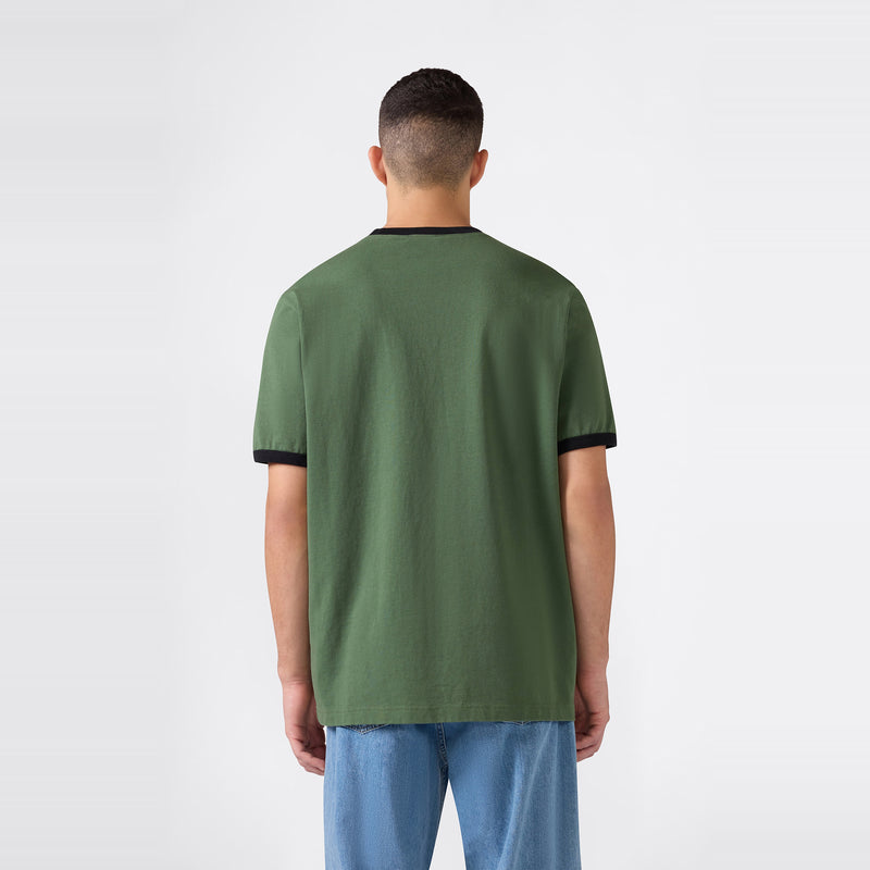 A man with short dark hair wearing a Champion Men’s Knitted Ringer T-Shirt in green with black trim and light blue jeans stands facing away against a plain white background.