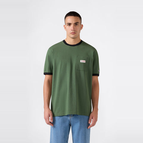 A person stands against a plain background, wearing a Champion Men’s Knitted Ringer T-Shirt in green with black trim and a chest pocket, paired with light blue jeans.